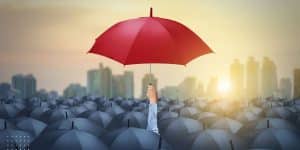 Man holding red umbrella in a cloud of black umbrellas grateful to find joy in the midst of adversity.