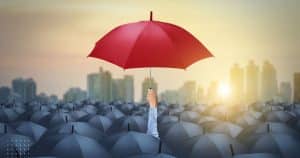 Man holding red umbrella in a cloud of black umbrellas grateful to find joy in the midst of adversity.